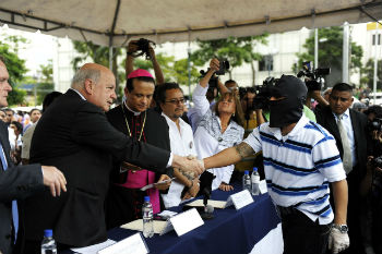 An OAS official shakes hand with a gang member as a Catholic bishop looks on
