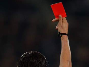 A soccer referee holds a red card, signifying a player is expelled from the game
