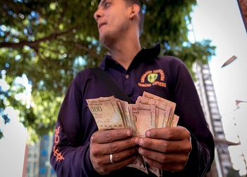 A man counting a stack of 100 bolivars bills