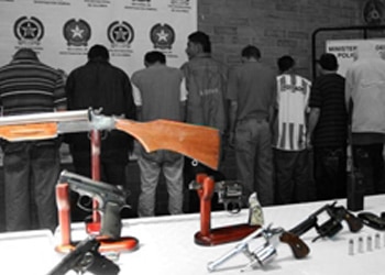 Seven Colombian drug traffickers facing a wall after being arrested, with a firearm in the foreground