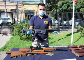 A member of the Ecuador police stands in front of a table, showing several trafficked firearms.
