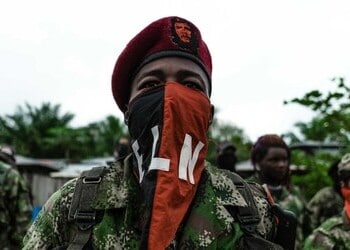 An ELN fighter stands with a mask emblazoned with his armed group's name.