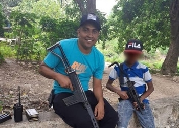 Carlos Enrique Gómez Rodríguez, alias "Conejo," holding a rifle next to a child, also armed