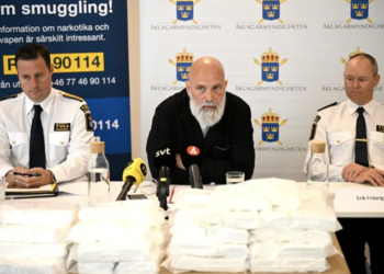 Three men give a press conference in front of bags of seized cocaine.