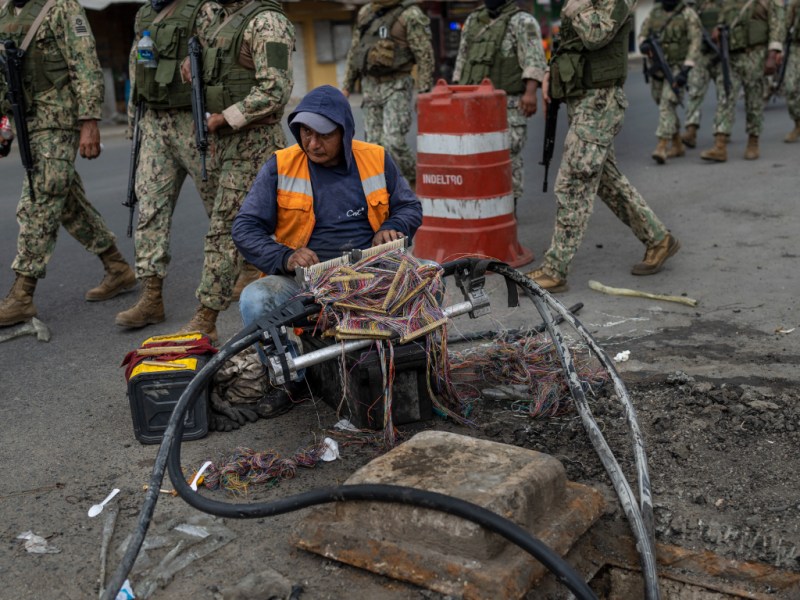 Soldiers march through Durán, Ecuador as man works on internet cables