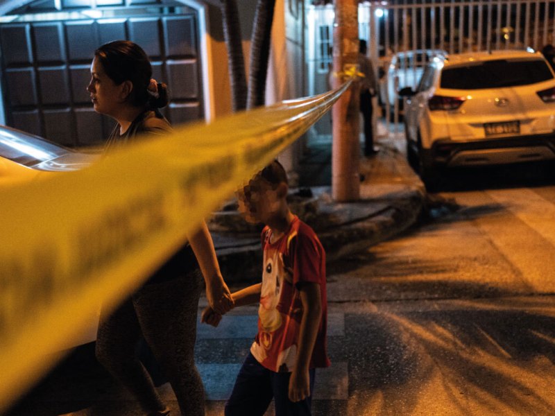 Un niño y una mujer caminan bajo la cinta policial que marca una escena del crimen en Guayaquil, Ecuador.