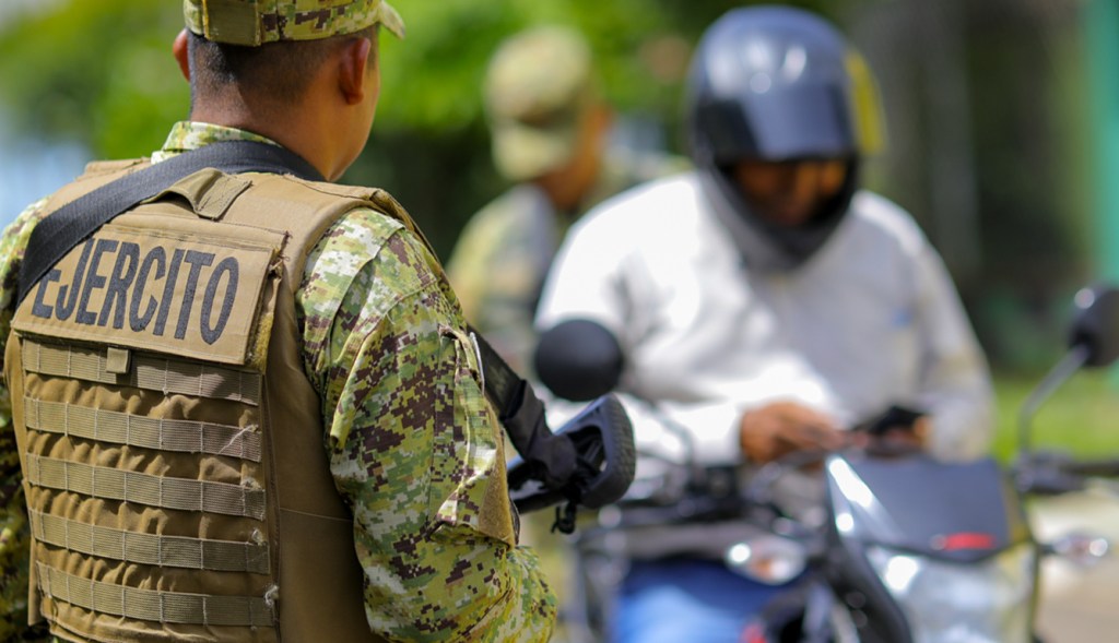 A member of El Salvador's armed forces stops a man on a motorcycle.