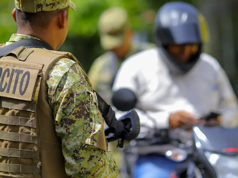 A member of El Salvador's armed forces stops a man on a motorcycle.