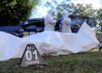 Authorities watch over a body in bodybag in Costa Rica, with a plaque in front of the body that read "OIJ 01 Cuerpo"