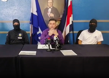 Two masked policemen sit on either side of their spokesperson as they criticize the government's approach to the security and homicide crisis.