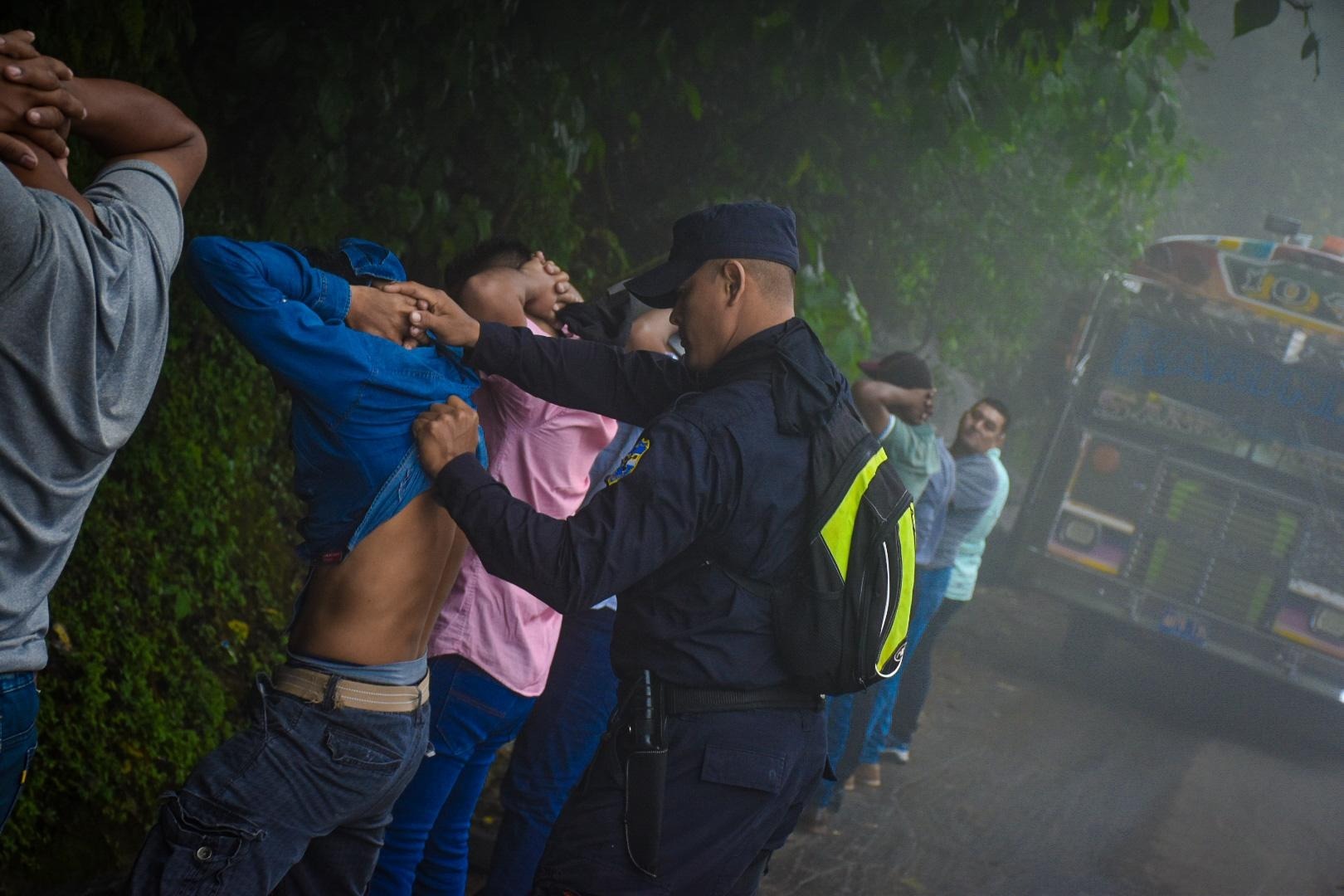 Salvadoran police detain and search men on the side of the road. 