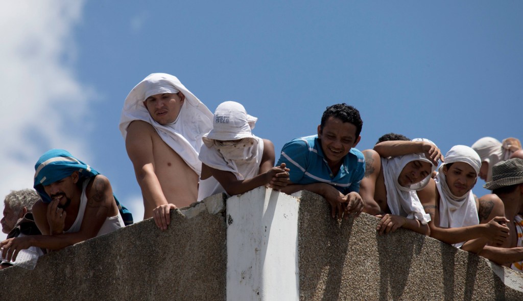 Presos venezolanos amotinados miran desde el tejado de un centro de detención dirigido por la Policía Nacional Bolivariana en Caracas, Venezuela.