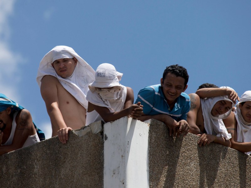Presos venezolanos amotinados miran desde el tejado de un centro de detención dirigido por la Policía Nacional Bolivariana en Caracas, Venezuela.