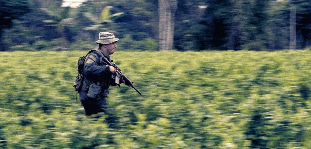 A soldier carrying a weapon running through a field of coca plants