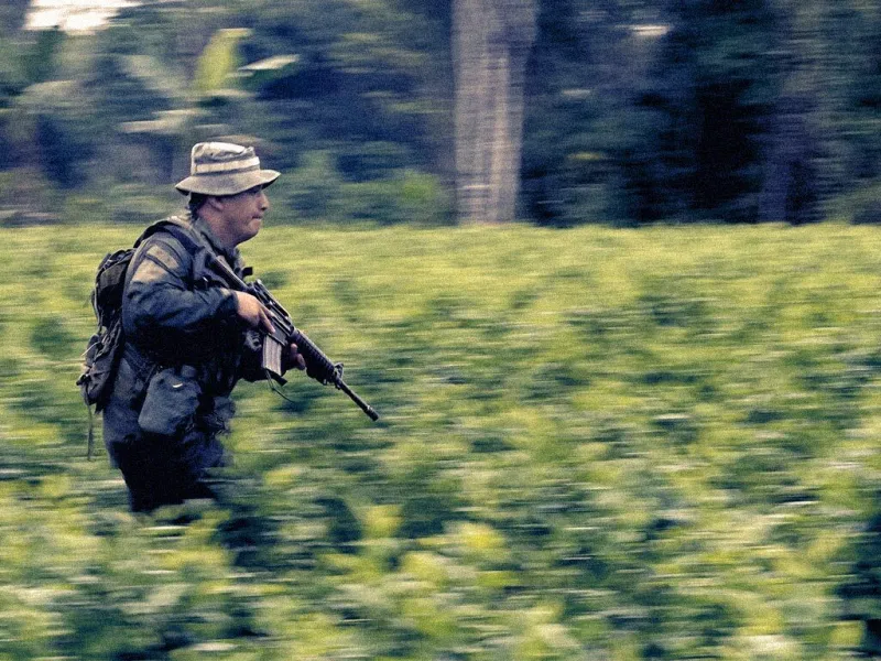 A soldier carrying a rifle running through a field of coca plants